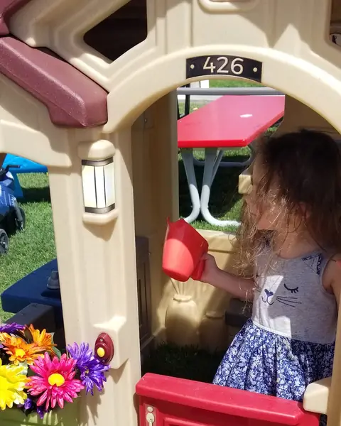 A child in a toy playhouse on the lawn, with flowers in its window boxes