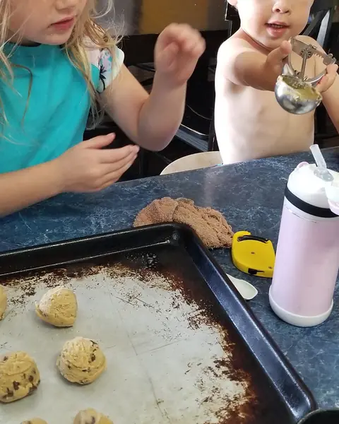 Two children with a tray of cookie dough at the kitchen table