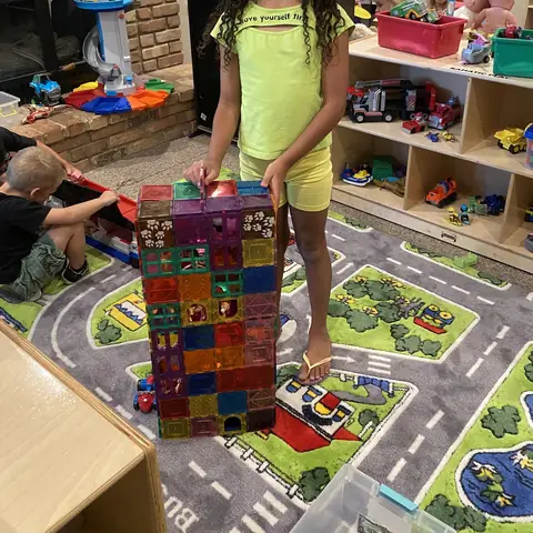 A playroom with a town-map rug, toy shelves and a tower of magnetic tiles